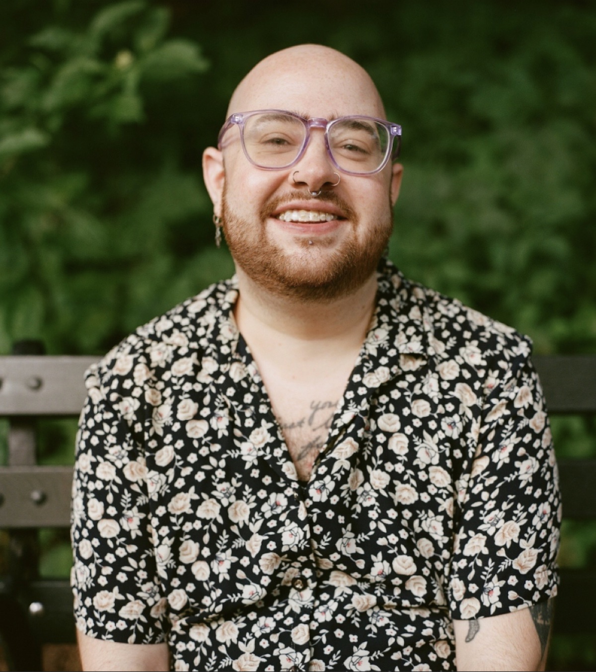 James Macaulay McManus, smiling, in glasses and a floral shirt on a park bench